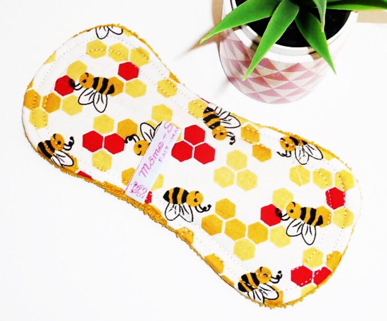 May include: A white cloth pad with a yellow honeycomb and bee pattern. The pad has a pink label that says "Mama - So Fat" on it.