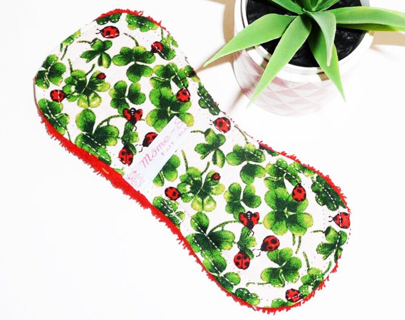 May include: A white cloth pad with a red border and a green four-leaf clover and ladybug print. The pad has a label that says "Mommy's" and "Fairy Magic".