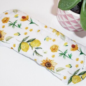 Peut inclure: Un protège-slip en tissu blanc avec un imprimé floral de citrons, de tournesols et de petites fleurs jaunes. Le protège-slip a un bord arrondi et est fait d'un tissu doux et absorbant.