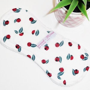 May include: White reusable cloth pad with a ladybug and leaf pattern. The pad has a white label with the text "Sweet-Mom" and "For Your Toi".
