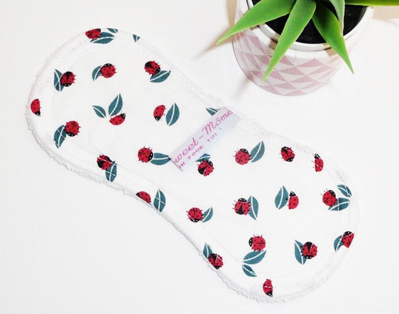 May include: White reusable cloth pad with a ladybug and leaf pattern. The pad has a white label with the text "Sweet-Mom" and "For Your Toi".
