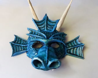 May include: A blue dragon mask with white horns and a textured surface. The mask has a detailed design with scales and fins.