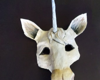 May include: A white unicorn mask with a long, pointed horn. The mask has black eye holes and a textured, sculpted face.