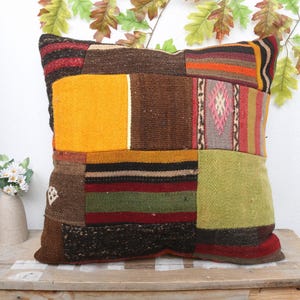 Pode incluir: Uma almofada de patchwork colorida com uma variedade de texturas e padrões, incluindo listras, desenhos geométricos e cores sólidas. A almofada é feita de lã e tem um visual rústico e feito à mão.