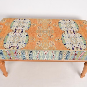 May include: A wooden bench with a colorful patterned cushion. The cushion has a geometric design with shades of orange, blue, red, and white.
