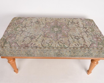 May include: A wooden bench with a floral patterned fabric top. The fabric has a light brown background with a multi-colored floral design.