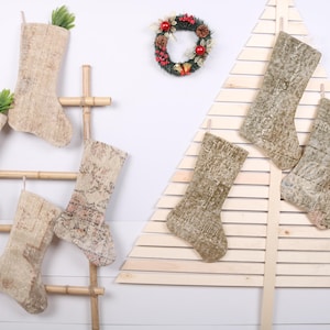 Pode incluir: Cinco meias de Natal de cor bege e marrom com padrão penduradas em uma escada de madeira e uma árvore de Natal de madeira. As meias são feitas de um tecido macio e felpudo.