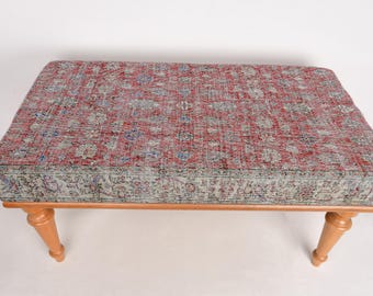 May include: A wooden bench with a red and blue patterned fabric top. The bench has four legs and a simple design.