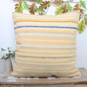 May include: A striped throw pillow with a cream background and yellow, blue, and gray stripes. The pillow has a subtle sheen and is made of a soft, woven fabric.