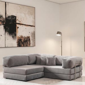 May include: A gray sectional sofa with a modular design. The sofa features a corduroy-like texture and includes several square throw pillows. The frame has a metallic accent. The sofa is in a modern living room setting.