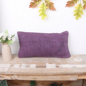 May include: A purple rectangular cushion with a textured surface sits on a wooden table. The cushion is in focus, and the table is out of focus.