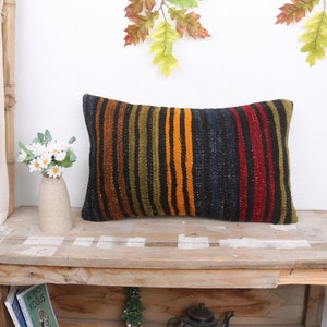 May include: A long rectangular pillow with a striped pattern in shades of brown, orange, red, and black. The pillow is sitting on a wooden table.