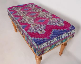 Puede incluir: Un banco de madera con patas de madera, tapizado con una alfombra kilim turca tradicional con motivos rosas, azules y blancos.