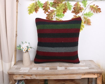May include: A striped throw pillow with red, black, green, and gray stripes. The pillow is on a wooden table with a vase of white flowers.