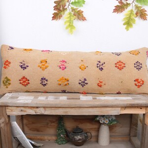 May include: A long, rectangular throw pillow with a beige background and colourful geometric patterns. The pillow is sitting on a wooden bench with a shelf underneath.