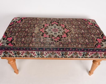 May include: A wooden bench with turned legs and a top upholstered with a colorful patterned fabric. The fabric features a central medallion design with floral motifs and a repeating geometric pattern.