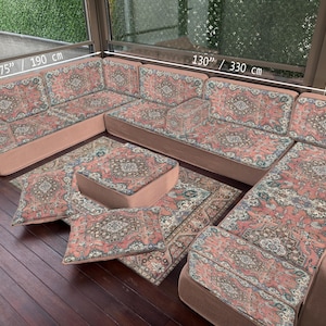 May include: U-shaped sectional sofa with a patterned rug and pillows. The sofa is 130 inches (330 cm) long and 75 inches (190 cm) wide. The rug and pillows have a red, beige, and blue floral design. The pillows are 28 inches (70 cm) wide.