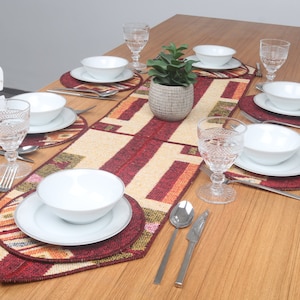 Puede incluir: Una mesa de madera preparada para una cena con platos blancos, cubiertos y vasos. La mesa está decorada con un mantel individual y caminos de mesa de color rojo, naranja y verde.