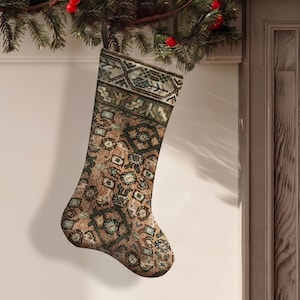 Puede incluir: Un calcetín navideño con un patrón tejido detallado y multicolor en tonos marrón, verde apagado y crema. El diseño incorpora intrincados motivos geométricos y florales que recuerdan a una alfombra, con un puño sólido en la parte superior.