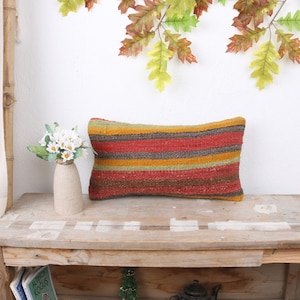 Pode incluir: Uma almofada longa e retangular com um padrão listrado em tons de vermelho, laranja, amarelo, verde e marrom. A almofada está sentada em uma mesa de madeira.