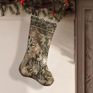 Puede incluir: Un calcetín navideño con un patrón complejo y multicolor en tonos óxido, marrón, crema y negro. El diseño incorpora intrincados motivos geométricos y florales que recuerdan a una alfombra tejida, con un lazo oscuro para colgar.
