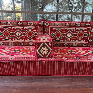 May include: A red and white patterned floor cushion with two matching back cushions and a smaller square cushion. The cushions are made of a woven fabric with intricate geometric designs.