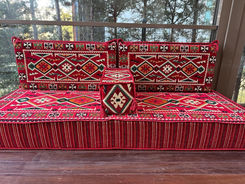 May include: A red and white patterned floor cushion with two matching back cushions and a smaller square cushion. The cushions are made of a woven fabric with intricate geometric designs.