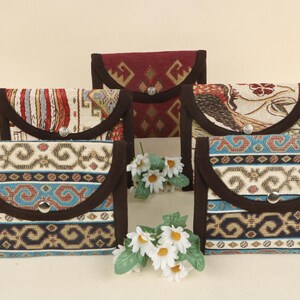 May include: Six fabric clutch purses with patterned designs. The purses display brown, cream, red, and blue hues. Each purse has a flap closure with a silver button. The purses are arranged in a group.