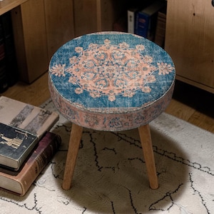 May include: A round accent table with a blue and peach patterned top and three wooden legs. The table has a vintage, distressed look, and is placed on a cream-colored rug.