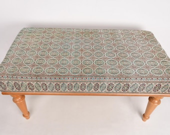May include: A wooden footstool with a patterned fabric top. The fabric is a light green and brown with a repeating circular design. The stool has four legs.