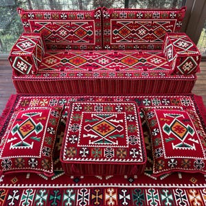 May include: A red and green patterned floor cushion set with a sofa, two square cushions, and a rectangular cushion. The cushions are all decorated with intricate geometric designs.