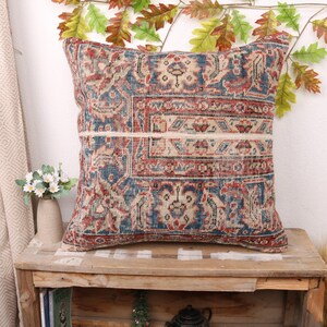 May include: A decorative pillow with a colorful, intricate pattern in shades of red, blue, and beige. The pillow is made from a woven fabric with a vintage look.