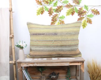 Può includere: Un cuscino a righe con uno schema di colori beige, verde e marrone. Il cuscino è appoggiato su uno scaffale di legno con altri oggetti decorativi.