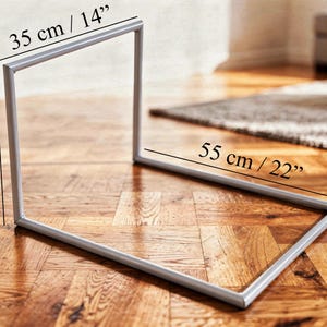 May include: A silver metal frame, 14 inches wide, 18 inches high, and 22 inches long, is displayed on a wooden floor. The frame is rectangular and appears to be a decorative or functional item.