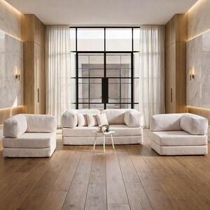 May include: A modern living room setup featuring a cream-colored sofa, two armchairs, and a small side table. The room has a large window, wooden floors, and marble accents, creating a bright and airy atmosphere.