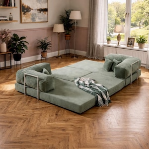 May include: A modular, sage green sofa with a modern design. The sofa is composed of several square cushions and two armrests with a silver metal frame. A patterned blanket rests on the sofa. The sofa sits on a hardwood floor.
