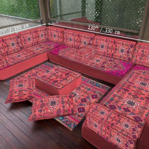 Warme koraalkleurige Majlis-bankset op vloer, rijke roodroze Turkse modulaire stoelen, ingewikkeld Koerdisch bloemenmedaillonpatroon, oosterse loungebank
