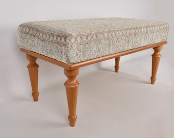 May include: A light wood footstool with a patterned fabric top. The footstool has four turned legs.