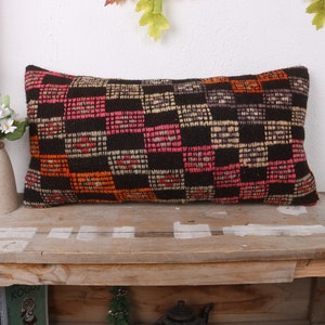 May include: A long rectangular pillow with a black, orange, pink, and white geometric pattern. The pillow is made of woven fabric and has a slightly textured surface.