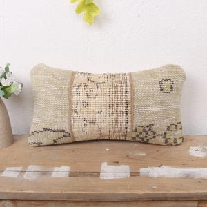 May include: A beige and brown patterned throw pillow with a rectangular shape. The pillow is made of woven fabric and has a subtle geometric design.