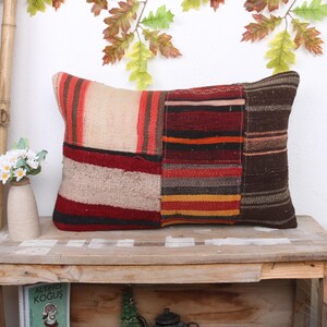 Op de afbeelding: Een rechthoekig kussen met een patchwork ontwerp in verschillende tinten rood, bruin, beige en oranje. Het kussen is gemaakt van geweven stof en heeft een rustieke, bohemian stijl.