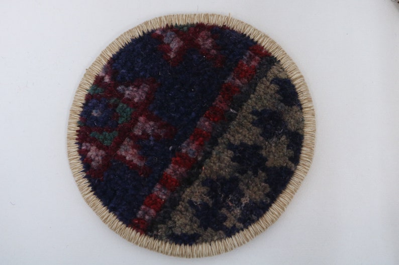 May include: A round, woven coaster with a colorful, geometric pattern in shades of red, blue, and green. The coaster has a natural, beige-colored border.