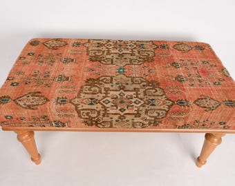 May include: A wooden ottoman with a red and brown patterned rug top. The ottoman has four legs and is made of wood.