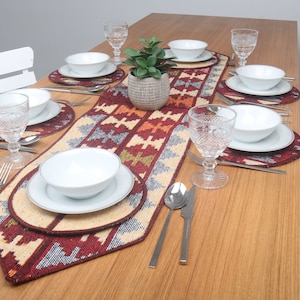 Puede incluir: Una mesa puesta con un camino de mesa estampado en rojo, blanco y azul. El camino de mesa está decorado con platos, cuencos y vasos blancos. Una pequeña planta en maceta se encuentra en el centro del camino de mesa.
