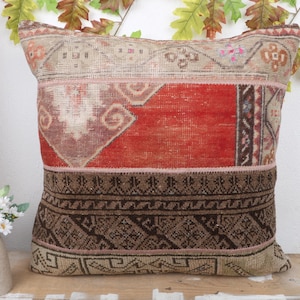 Può includere: Cuscino decorativo quadrato con un design patchwork. Il cuscino presenta un mix di colori, tra cui rosso, marrone e beige, con motivi geometrici e floreali. Il cuscino è realizzato in un tessuto strutturato, probabilmente un tappeto o un arazzo.