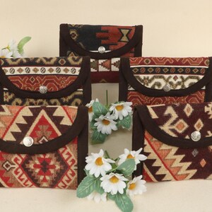 May include: Five rectangular, patterned fabric pouches with a flap closure and a silver button. The pouches feature a brown border and a Southwestern-inspired design in red, tan, and brown. White flowers are in the foreground.
