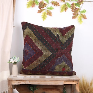 May include: A decorative throw pillow with a geometric pattern in shades of burgundy, gold, black, and purple. The pillow is sitting on a wooden shelf.