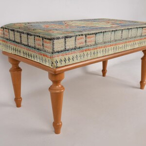 K&ouml;nnte beinhalten: Ein Hocker aus Holz mit einer gemusterten Stoffoberfl&auml;che. Der Stoff ist eine Mischung aus blauen, gr&uuml;nen und orangen Farben. Der Hocker hat vier gedrehte Beine.