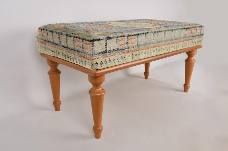 K&ouml;nnte beinhalten: Ein Hocker aus Holz mit einer gemusterten Stoffoberfl&auml;che. Der Stoff ist eine Mischung aus blauen, gr&uuml;nen und orangen Farben. Der Hocker hat vier gedrehte Beine.