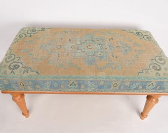 May include: A light brown wooden bench with a blue and beige patterned cushion. The cushion has a floral design.